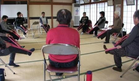 こつこつクラブの参加者が椅子にすわり、セラバンドを使って足の筋力を鍛える体操をしている様子。